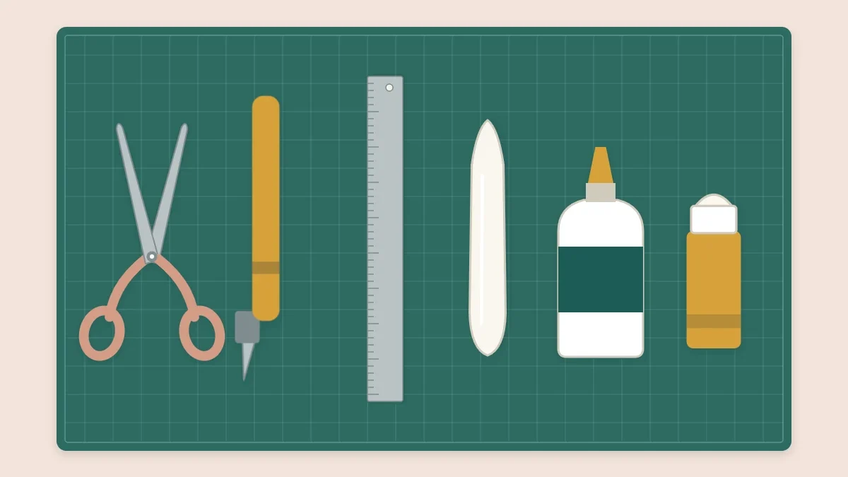 Scissors, a craft knife, a metal ruler, a bone folder and glue laid out in a row on a cutting mat
